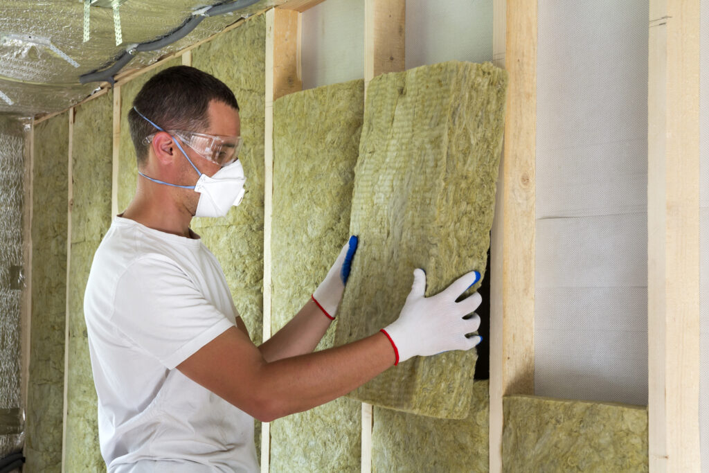 worker in protective goggles and respirator insulating rock wool