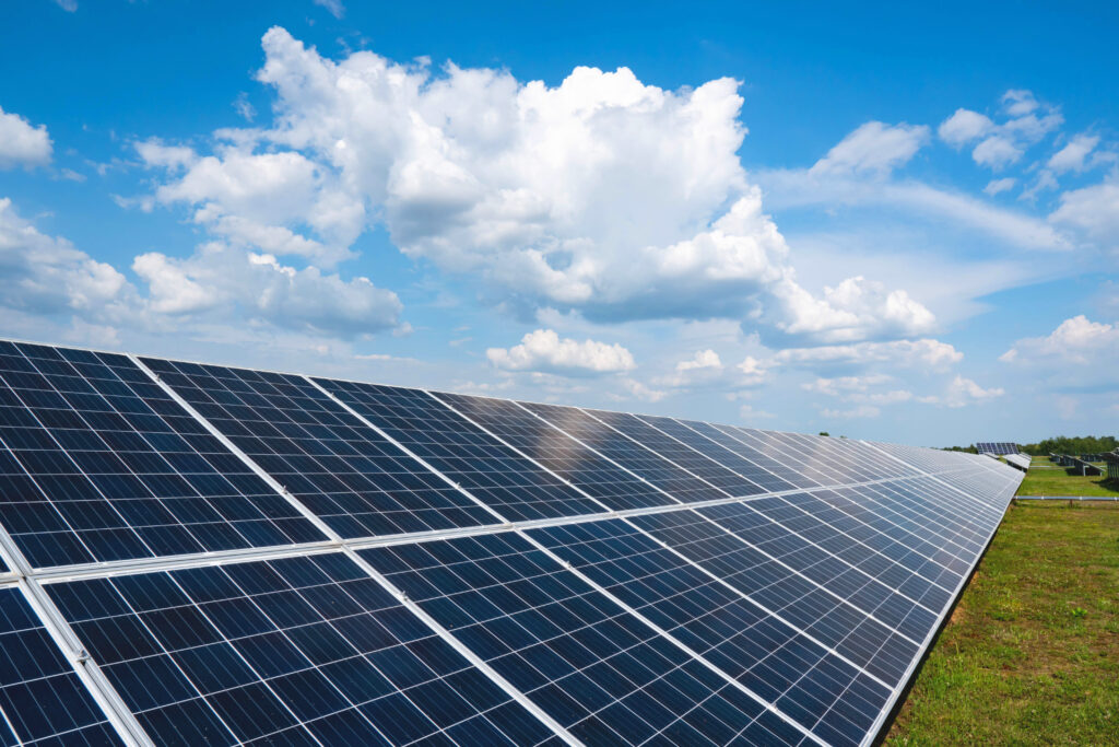 a row of solar panels in a field with clouds and a blue sky. green energy production.